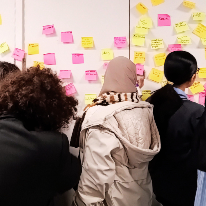 A group of teenagers from the Nova Youth Voice Group stand in front of a wall containing numerous post-it notes with ideas written on it, the group is voting which causes they should support